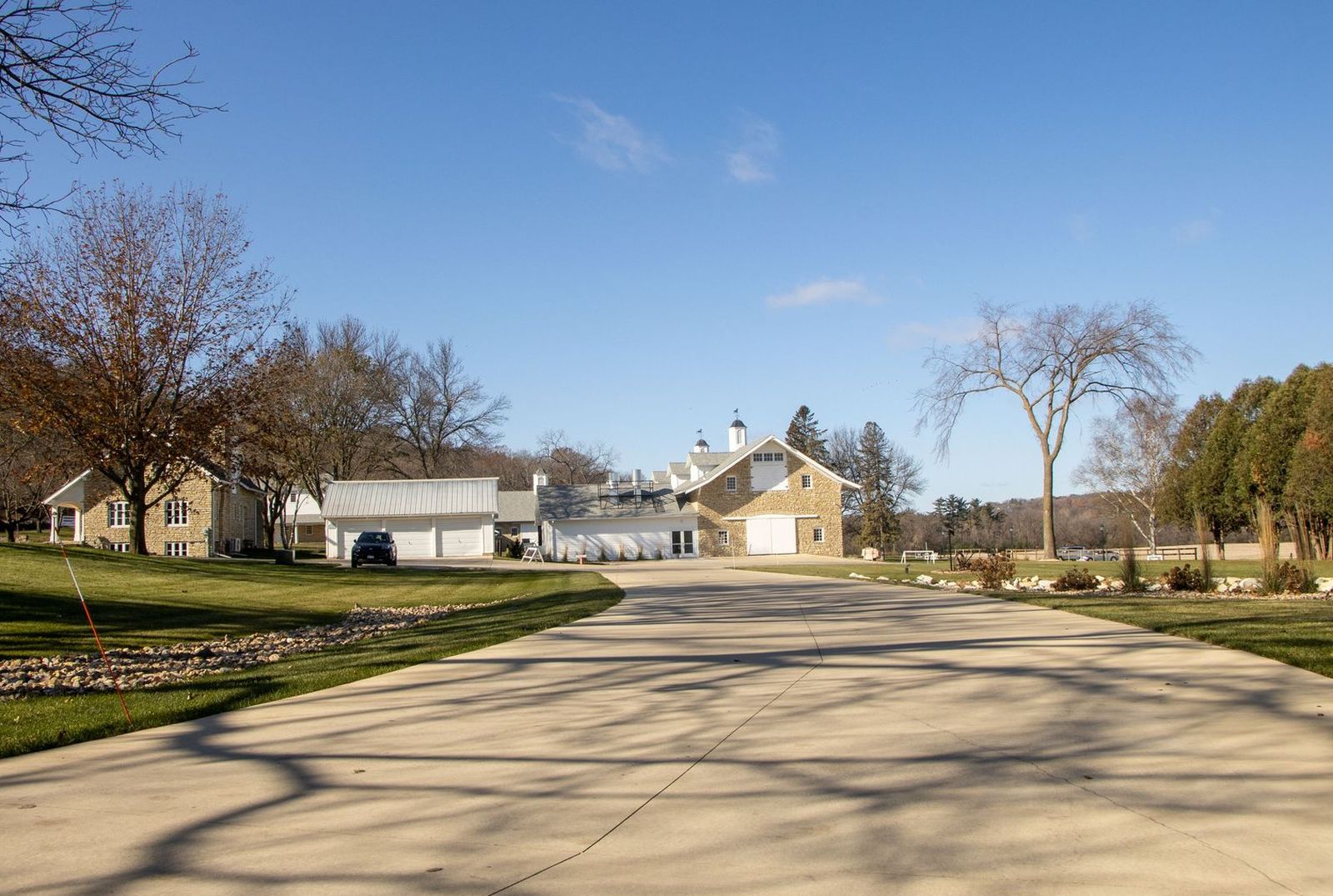 Long concrete driveway leading to a stone house and outbuildings on a large lot