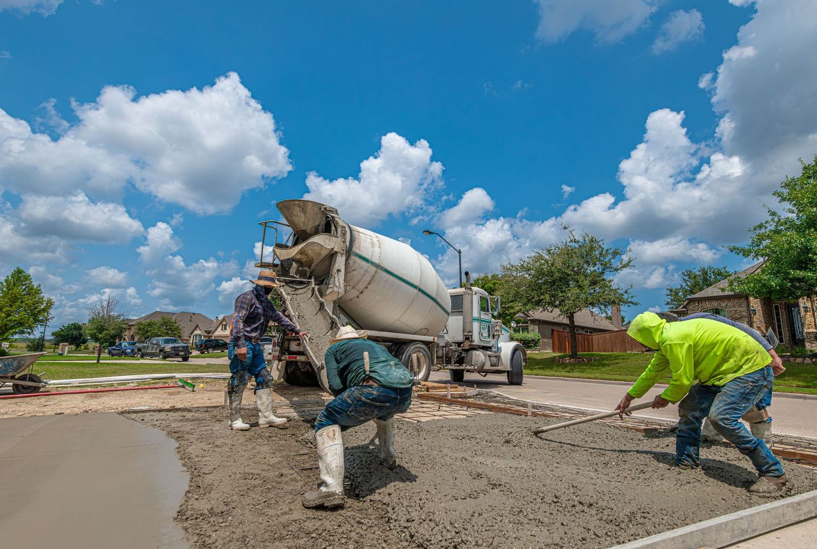Concrete crew raking a fresh residential driveway pour from a mixer truck in a Texas subdivision