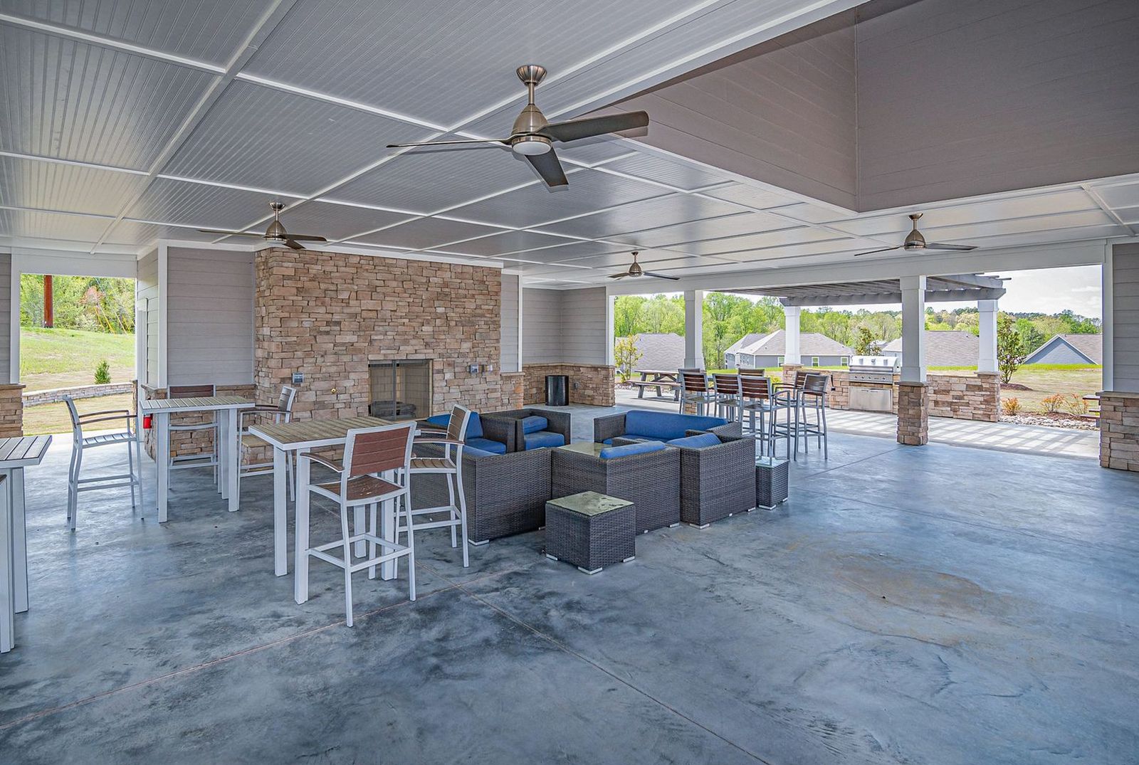 Large concrete patio under a covered pavilion with seating and a stone fireplace