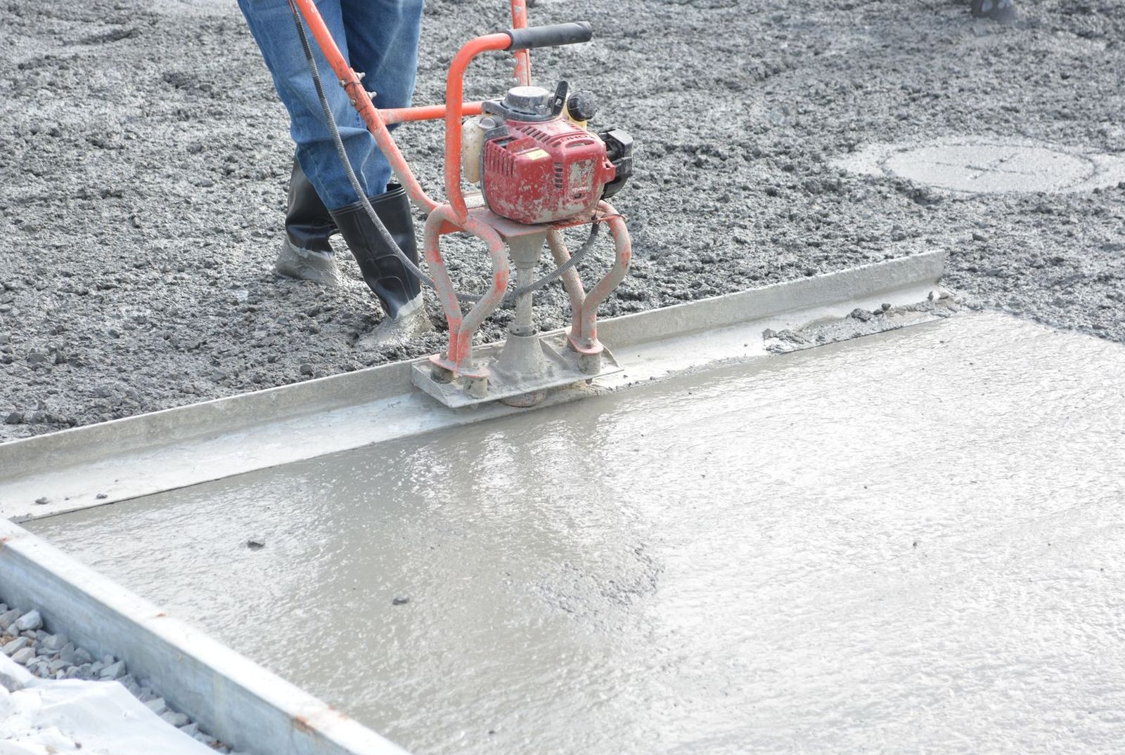 Power screed leveling wet concrete across a formed slab