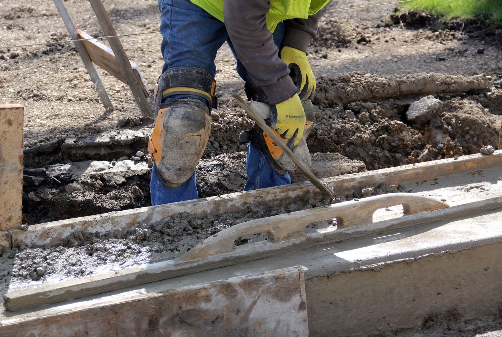 Concrete finisher running an edger along the formed edge of a fresh sidewalk pour