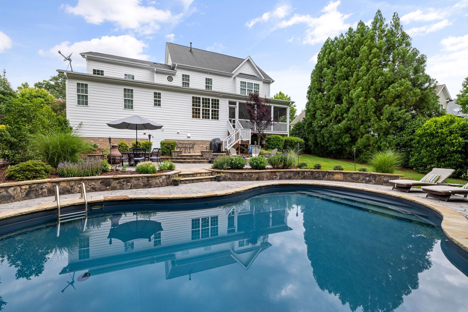 Stamped concrete pool deck in a flagstone pattern around a curved pool behind a two-story house