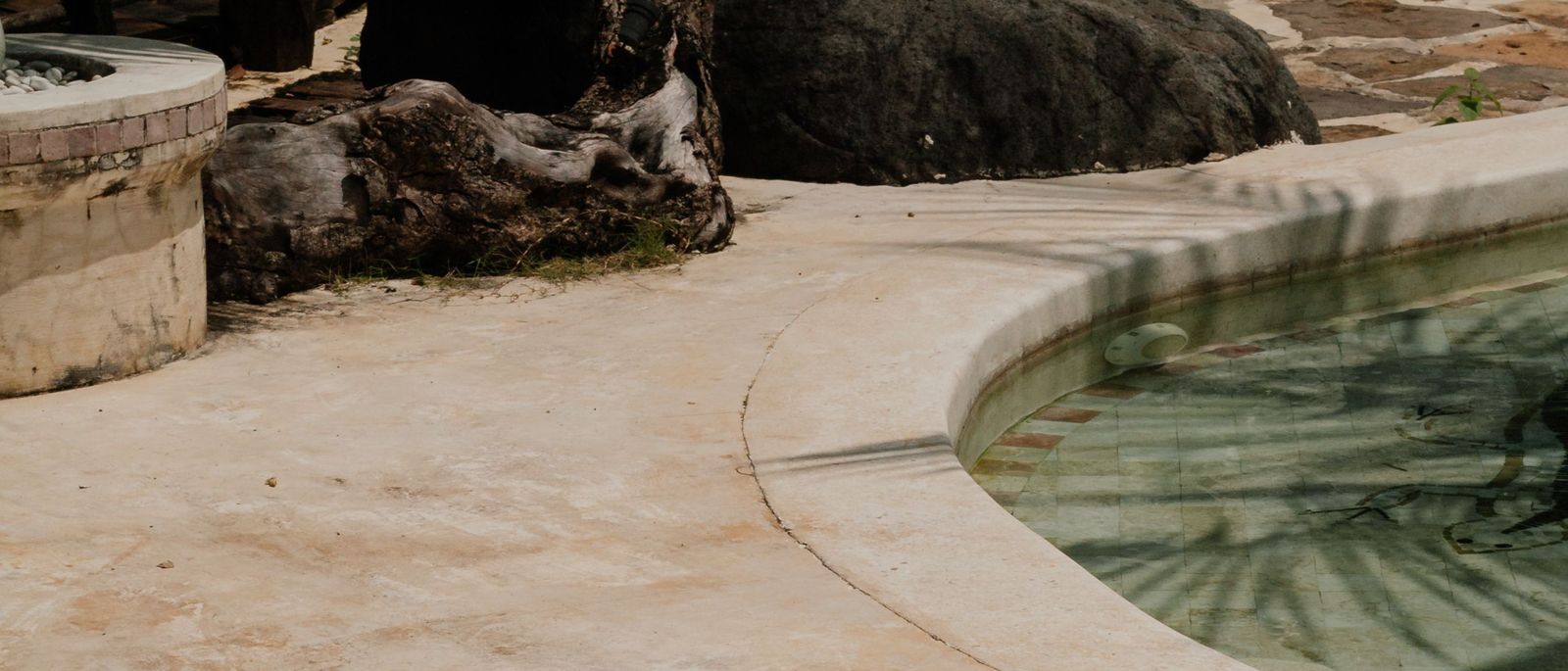 Weathered, faded concrete pool deck along a curved coping edge